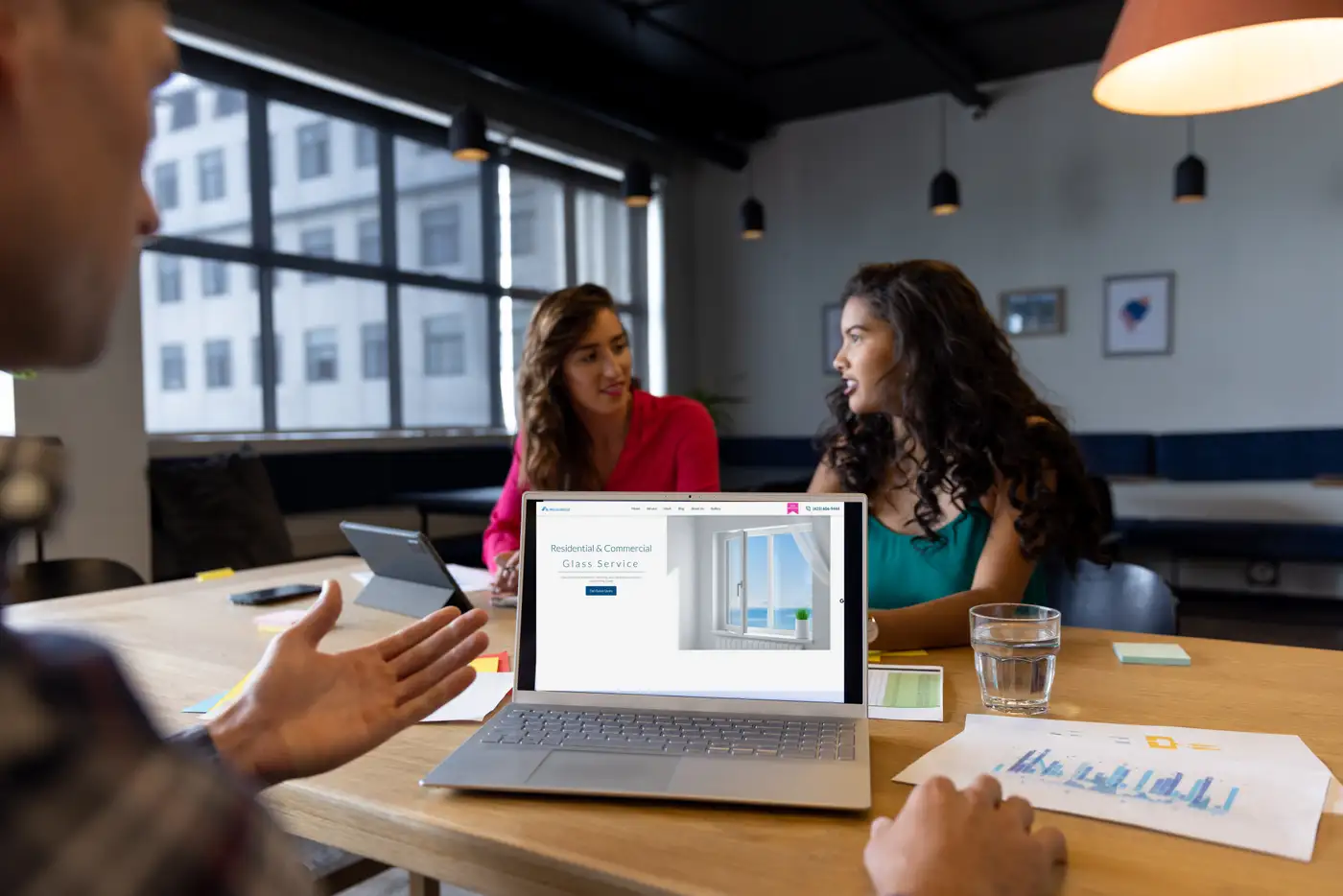 Agency team reviewing a client website on a laptop in a meeting; the screen shows the Aria Glass homepage built by RankMeHi
