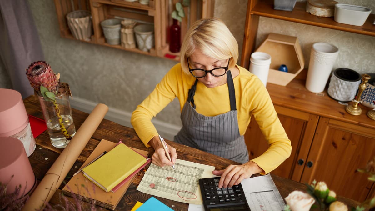 Shop owner working out monthly costs with a calculator and paper bills