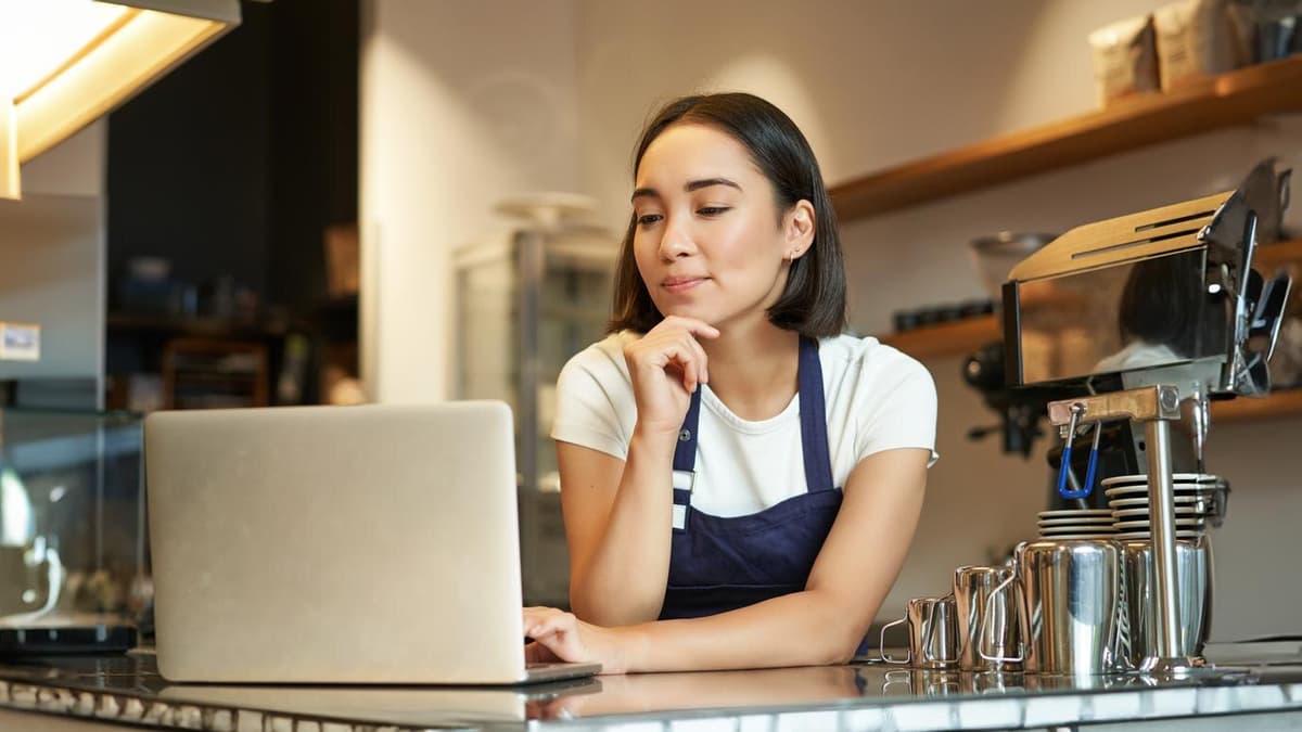 Cafe owner at the counter working on her business listing on a laptop