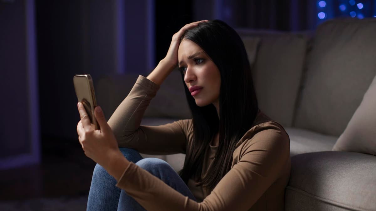 Woman on a sofa late in the evening frowning at her phone