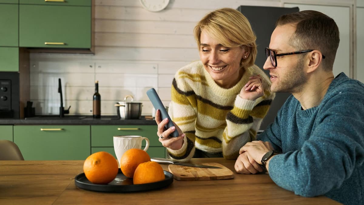 Woman showing her husband an answer on her smartphone in their kitchen