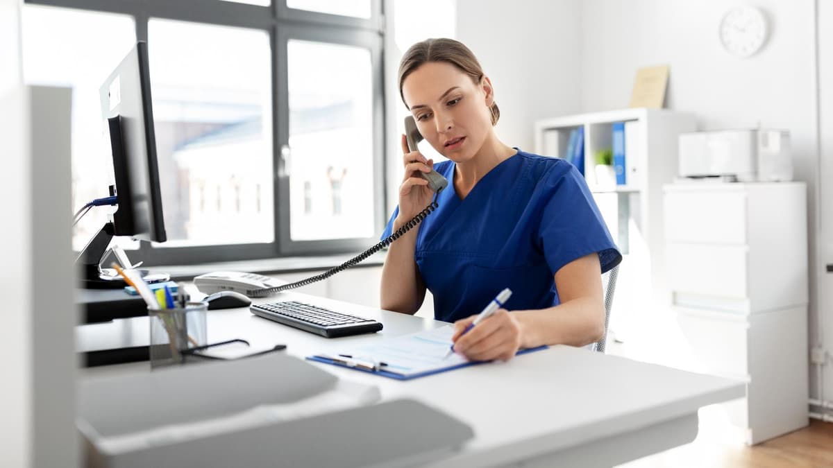 Practice staff member on the phone at the front desk taking notes on a clipboard