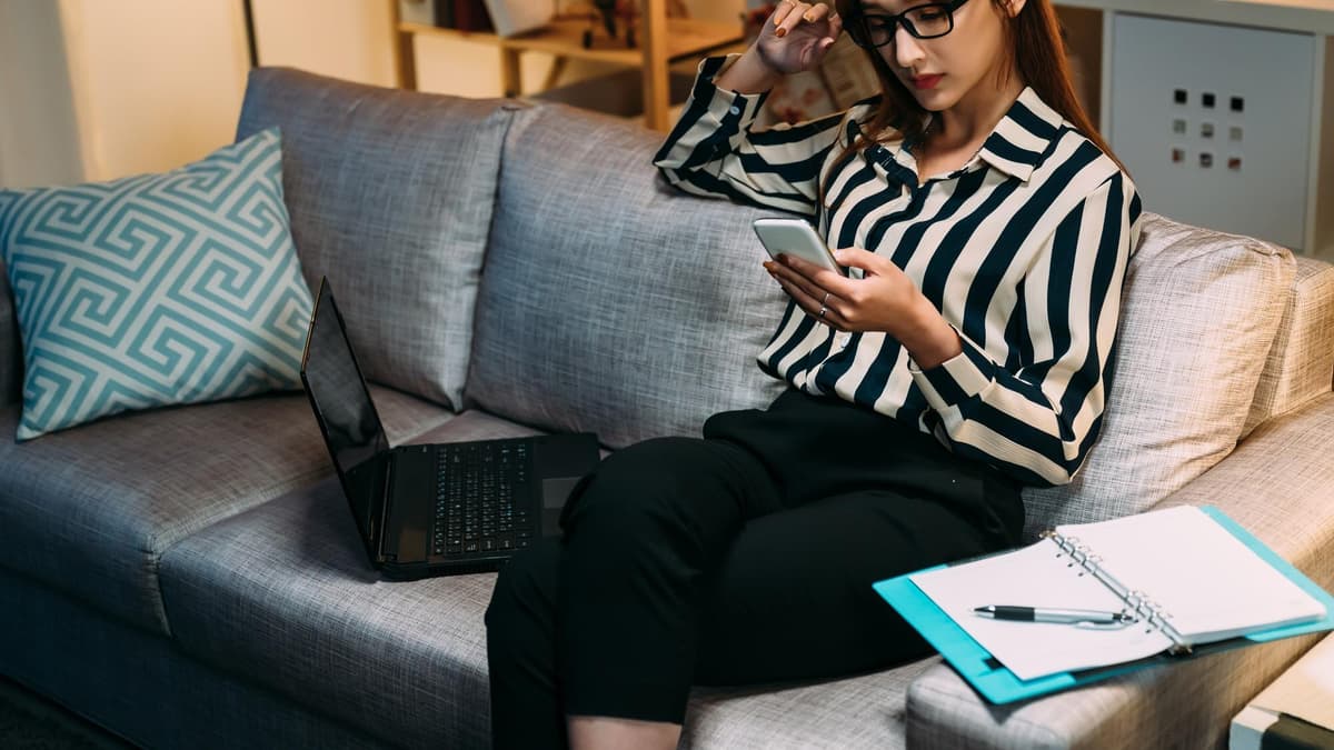 Woman on a couch at night reading messages on her phone with a worried look