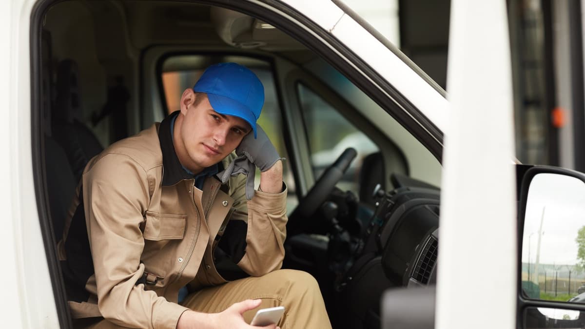 Tradesman in uniform sitting in his van holding a phone