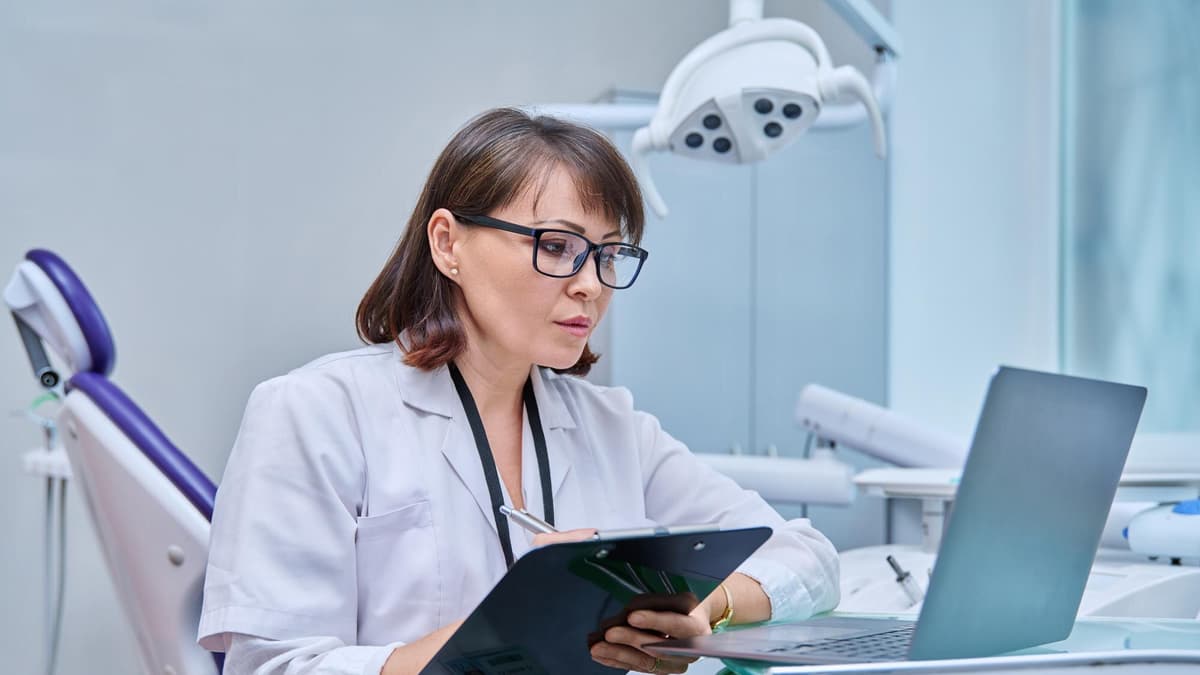 Dentist making notes on a clipboard next to the dental chair and a laptop