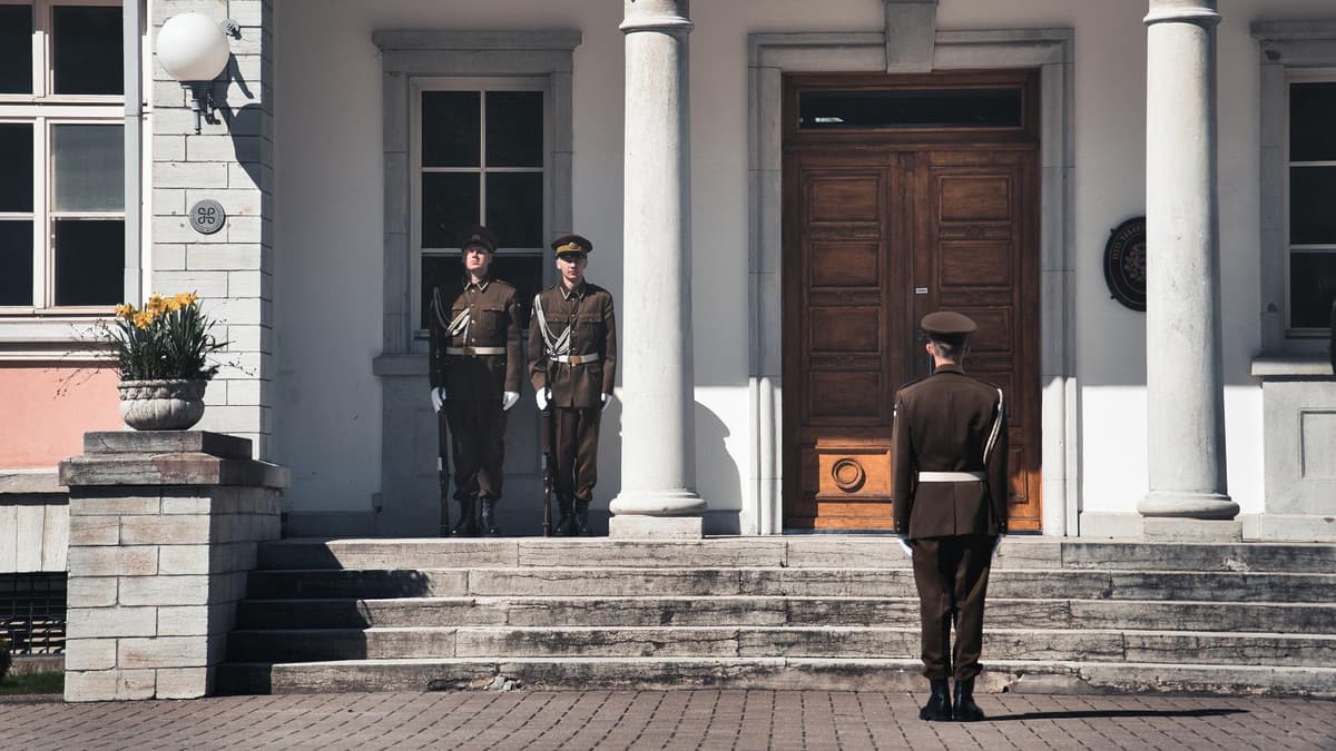 Two uniformed guards stand at the front door of a classic columned building
