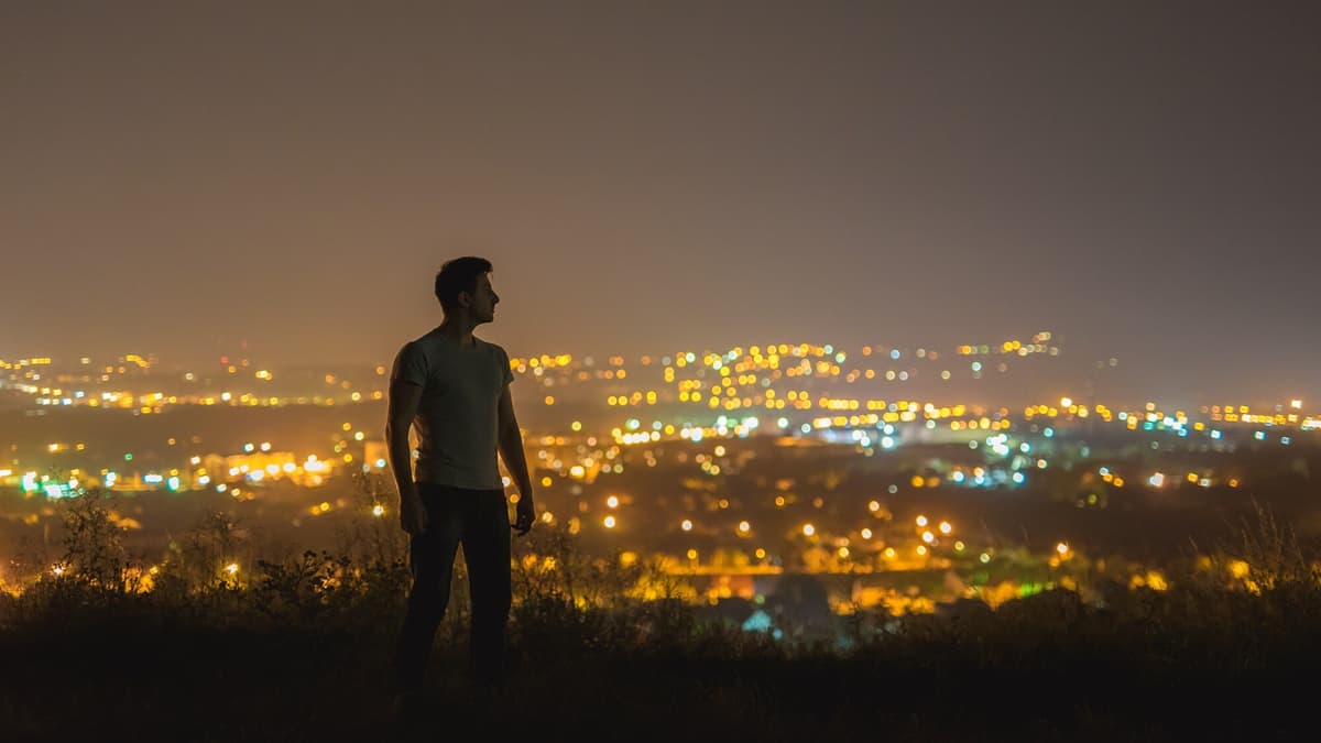 Man standing on a hill at night looking out over the lights of the next town