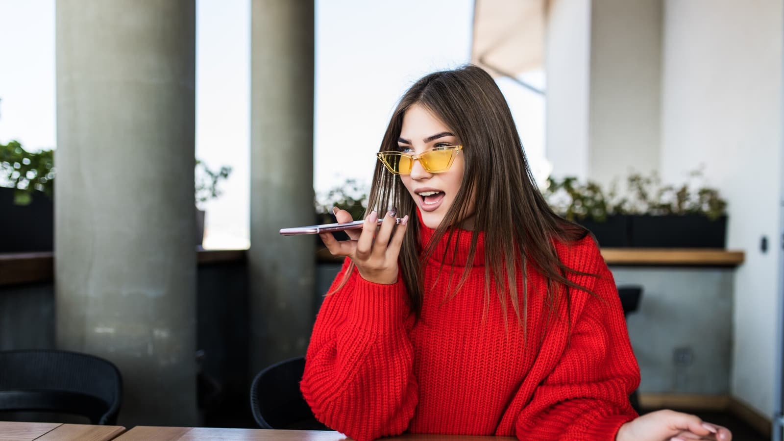 Business owner asking a voice assistant a question on her phone in a cafe, the everyday face of answer engine optimization