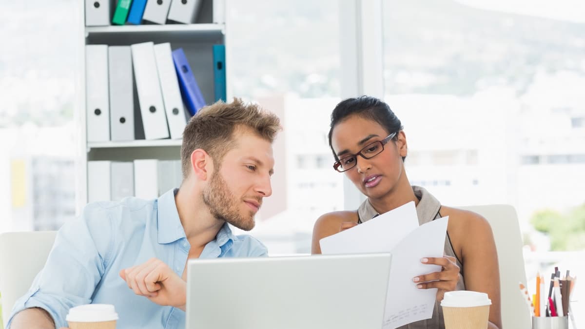 Two colleagues reviewing figures in a spreadsheet on a laptop at a meeting table