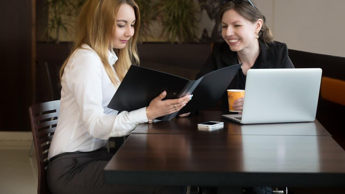 Small business owner and a web developer reviewing a laptop together at a bright cafe table