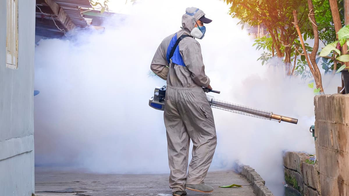 Pest control technician treating the outside of a house during a scheduled service