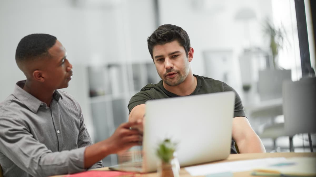 Two marketers reviewing keyword research on a laptop in a small agency office