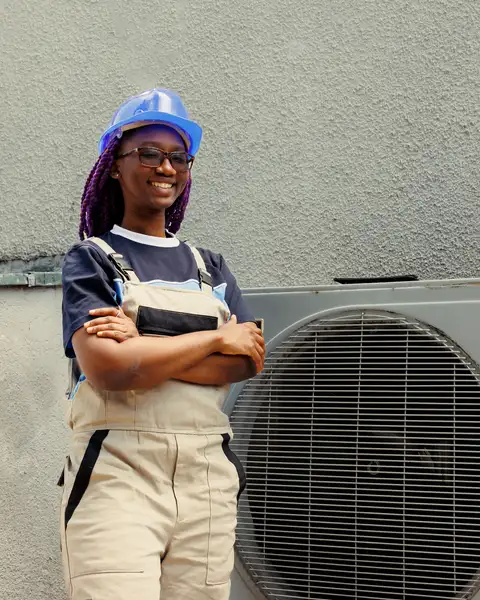An HVAC technician stands beside an outdoor air conditioning unit