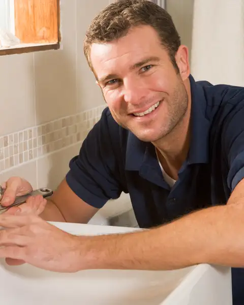 A plumber fitting a bathroom tap smiles at the camera