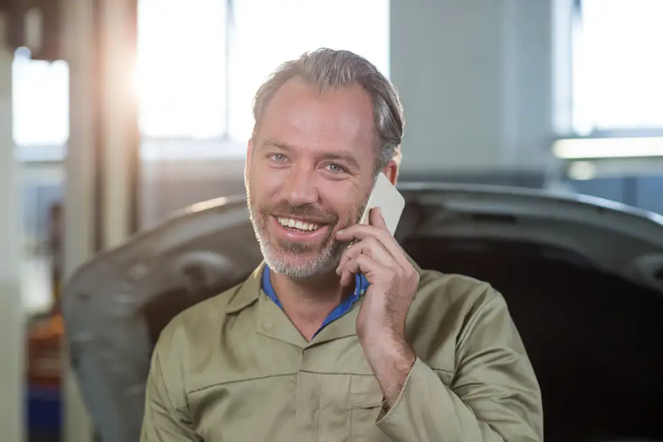 A mechanic smiles while taking a customer call in his workshop