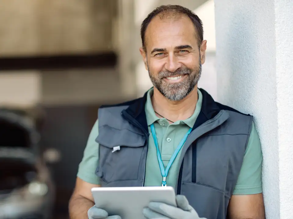 A smiling mechanic holds a tablet in his workshop