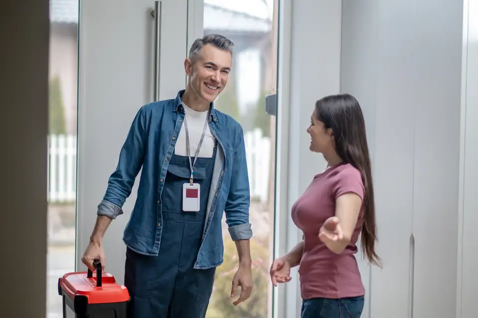 A homeowner opens her front door to a tradesman carrying a toolbox