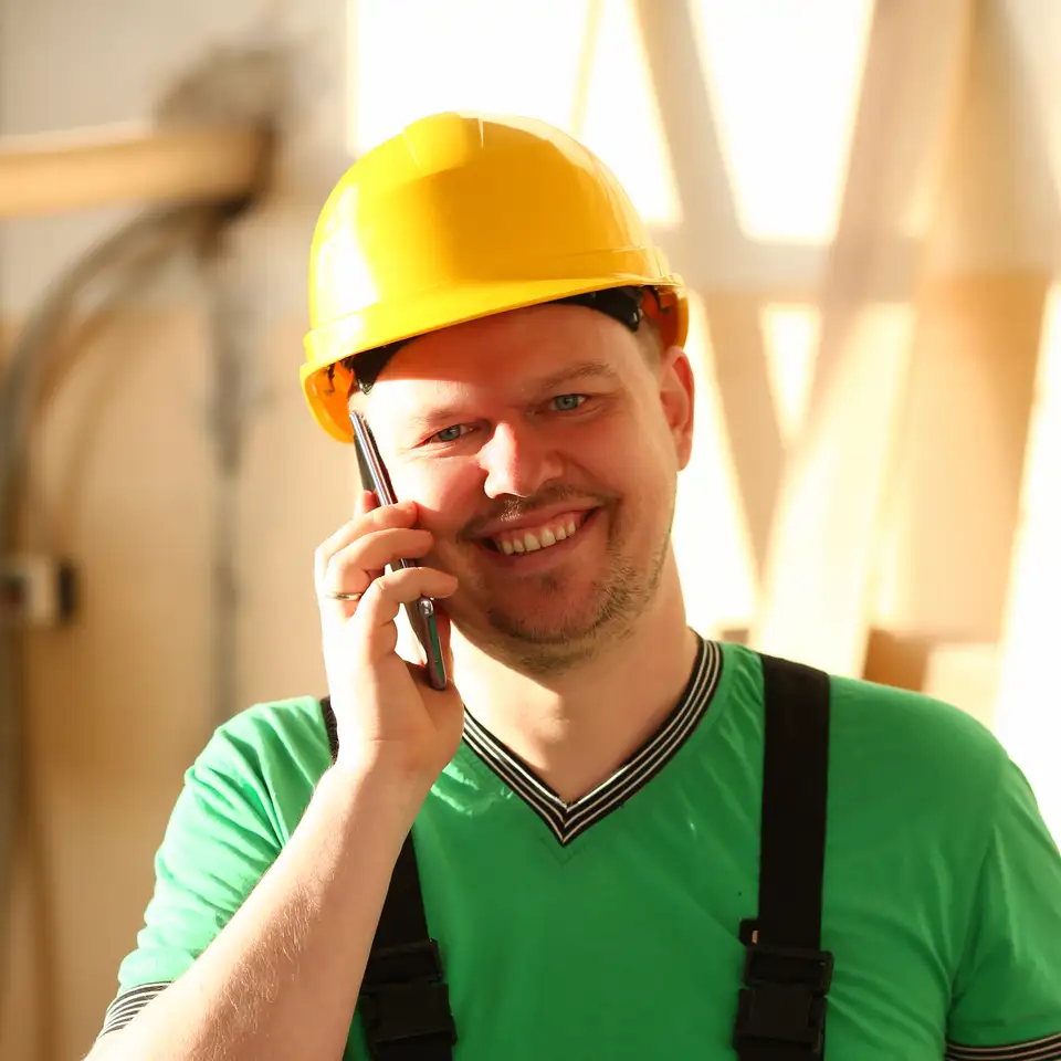 A tradesman in a hard hat smiles as he takes a call and writes down the job