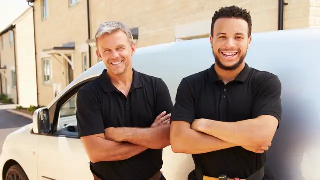 Two tradesmen stand with arms crossed beside their work van
